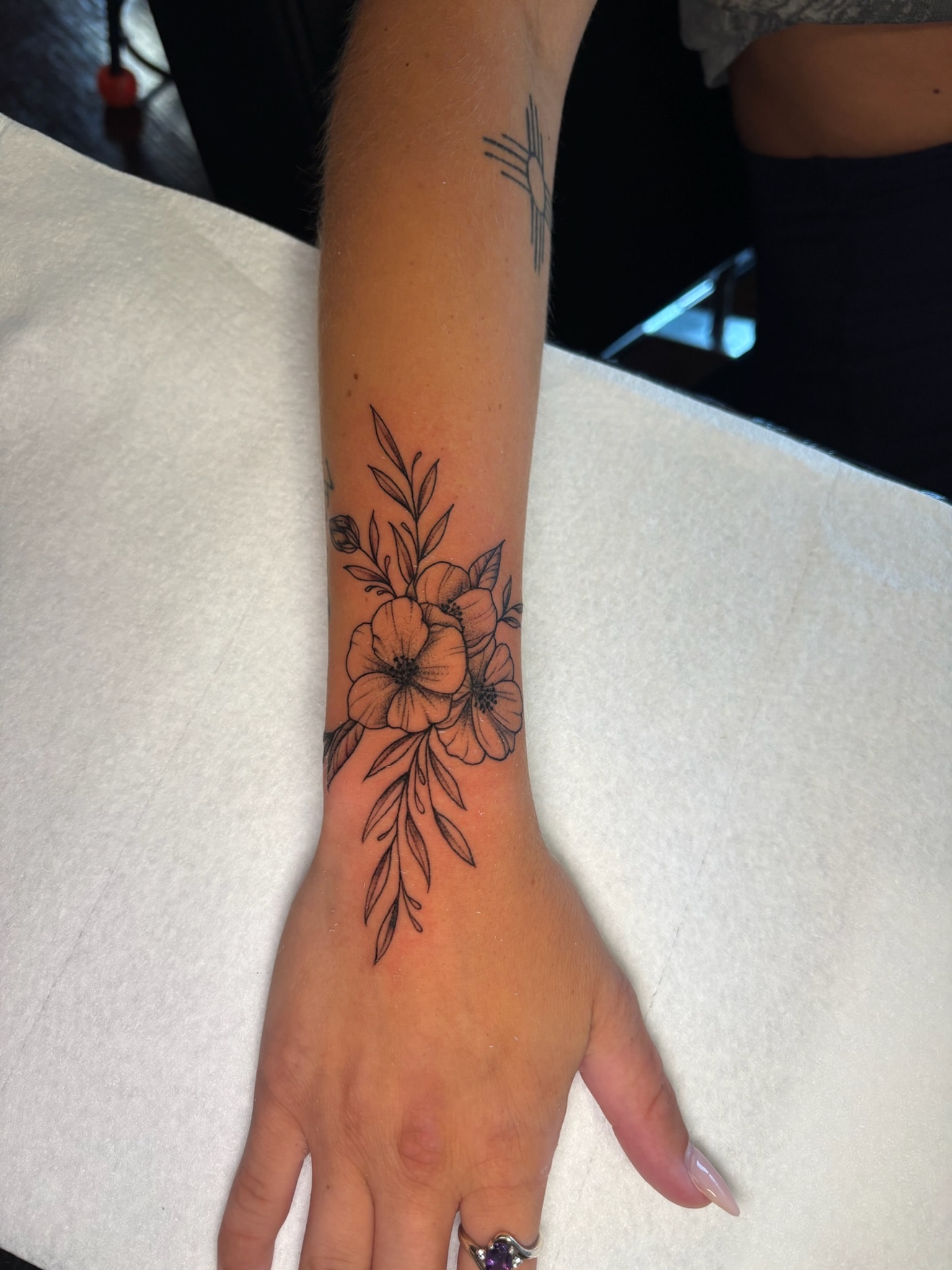 Fine line floral bouquet wrist tattoo with poppies and botanical leaves