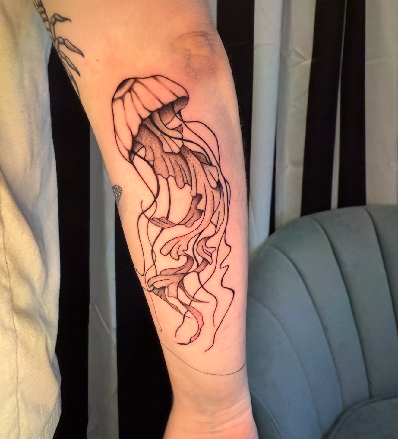 Fine line jellyfish tattoo on forearm with flowing tentacles